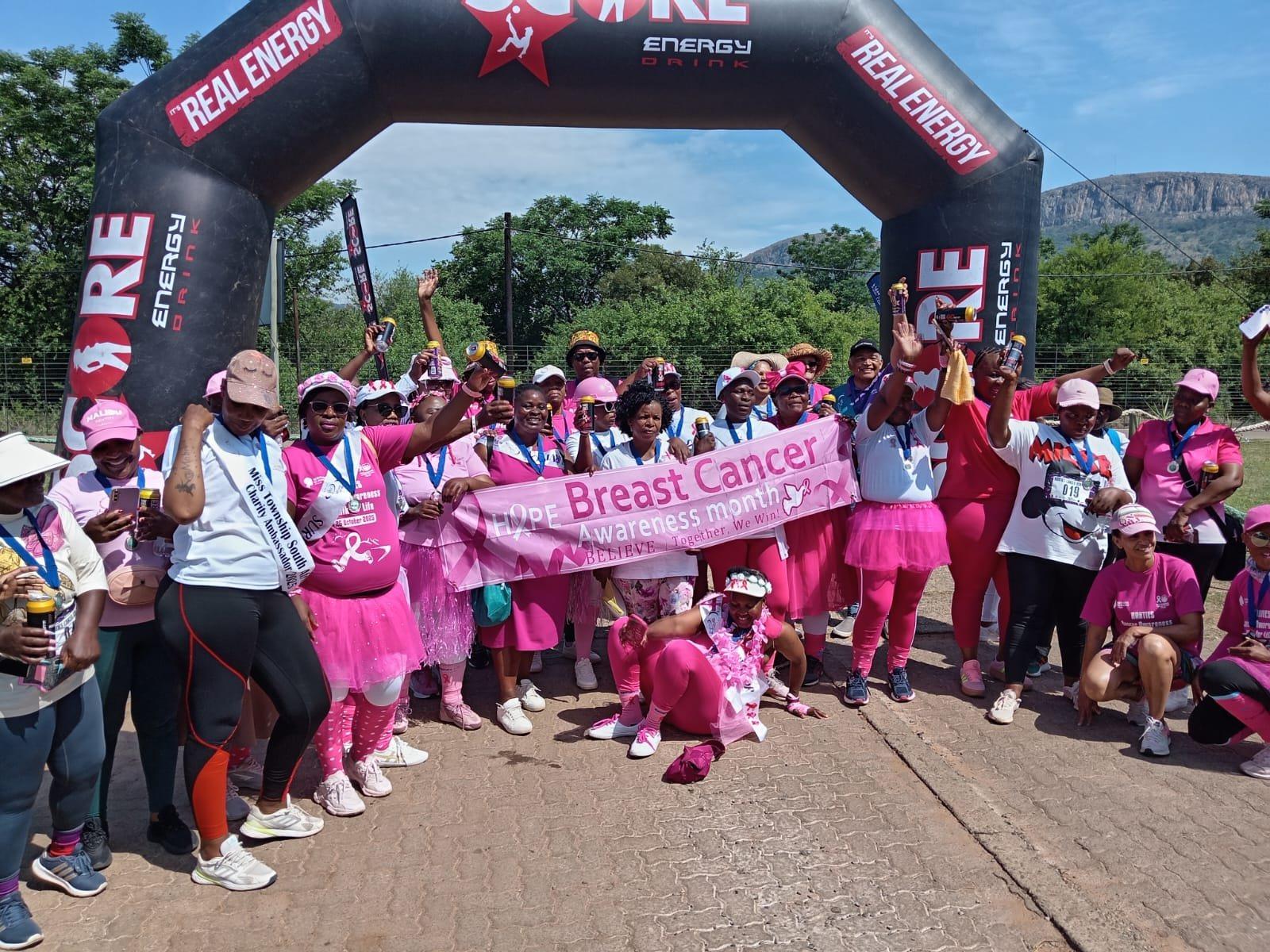 A joyful crowd of South African women in pink at a Breast Health Foundation awareness walk, holding a banner reading Hope, Breast Cancer Awareness Month, Together We Win.